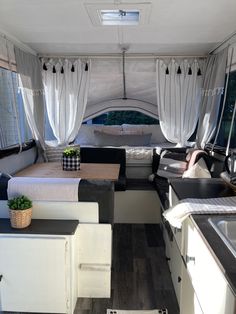 the interior of a camper with white curtains and black counter tops, wood flooring