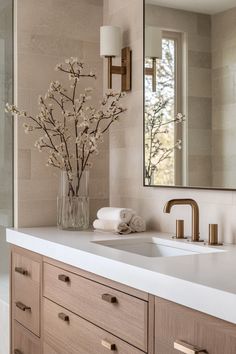 a bathroom with a sink, mirror and flowers in a vase on the counter top