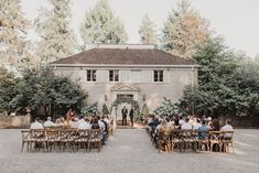 a group of people sitting at wooden tables in front of a large building with trees