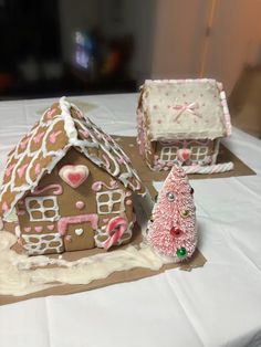 two gingerbread houses on a table with white tablecloths and pink decorations in the shape of hearts