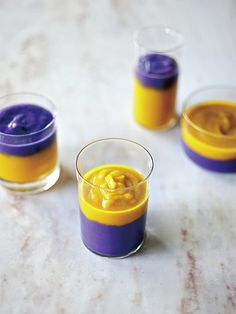 three small glasses filled with yellow and purple liquid on top of a white countertop