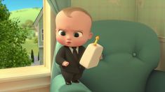 a baby in a suit is holding a bottle and looking at the camera while standing next to a green chair