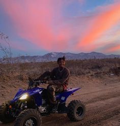 a man riding on the back of a blue four - wheeled vehicle down a dirt road