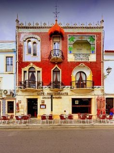 an old building with chairs and tables in front of it on the side of the road