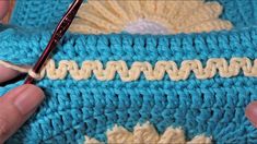 someone is crocheting the edges of a blue and yellow afghan with a red handled crochet hook