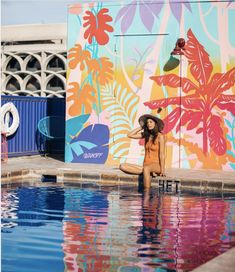 a woman sitting on the edge of a swimming pool in front of a colorful wall