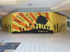 a large mural in the middle of an airport lobby with people walking around and holding hands