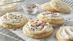 cookies with white frosting and sprinkles on a cooling rack next to a bowl of whipped cream