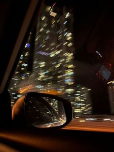 a car's rear view mirror is shown in the night time scene with buildings lit up