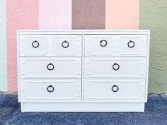 a white dresser with four drawers in front of a multicolored wall