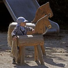 a small child sitting on top of a wooden bench next to a playground equipment slide