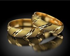 two gold wedding rings sitting next to each other on a black surface with reflections in the background