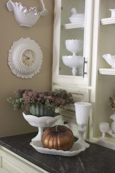 a kitchen counter topped with dishes and vases next to a clock on the wall