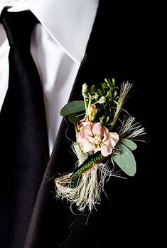 a boutonniere with flowers and feathers is worn on a man's black suit