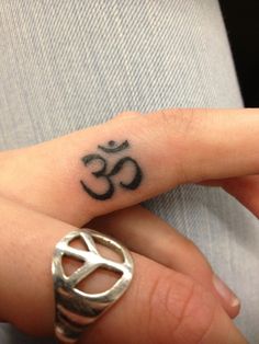 a woman's hand with a small tattoo on the middle finger and an om symbol in the middle