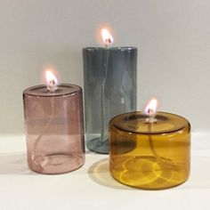 three different colored candles sitting next to each other on a white surface with one burning