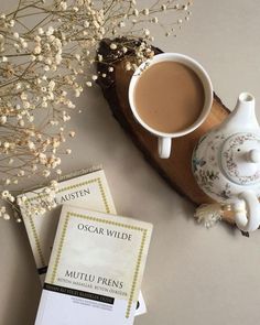 there is a cup of coffee next to some books and a vase with flowers on it