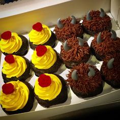 there are many cupcakes with yellow frosting and red flowers on them in the box