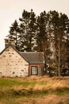 an old stone house in the middle of a field with trees around it and grass on the ground