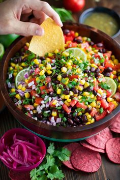 a person dipping a tortilla into a bowl filled with black beans and corn