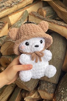 a small white teddy bear wearing a brown hat and scarf sitting on top of logs