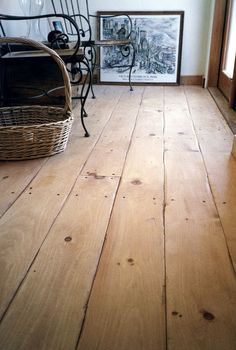 a wooden floor in a room with pictures on the wall and a wicker basket next to it