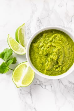 guacamole in a white bowl surrounded by limes and cilantro