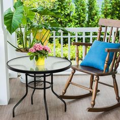 two wooden rocking chairs sitting on top of a porch next to a table with flowers