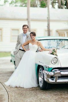 a bride and groom standing next to an old car