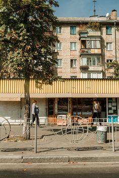 people are walking on the sidewalk in front of an apartment building with bicycles parked outside