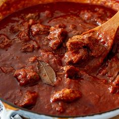 a wooden spoon in a pot filled with meat and tomato sauce on top of a table