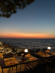 an outdoor dining area next to the ocean at dusk with lit candles and place settings