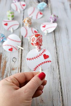 a hand holding up a baseball shaped lollipop with hearts on it and candy in the background