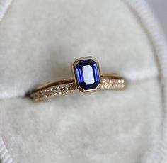 an engagement ring with a blue stone in the center on a white velvet cushioned surface