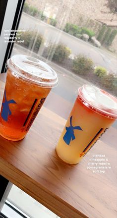 two drinks sitting on top of a wooden table next to a window with a view