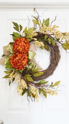 a wreath with orange flowers and green leaves hangs on the front door's white door