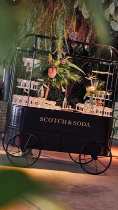 a black cart with plants in it sitting on the ground next to a building and trees