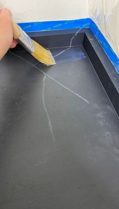 someone using a brush to paint the bottom of a black tray with blue tape on it