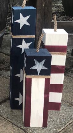 three wooden blocks with stars and stripes painted on them, tied to ropes in front of a tree