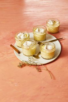 four small desserts on a plate with a wooden spoon and some dried herbs next to them