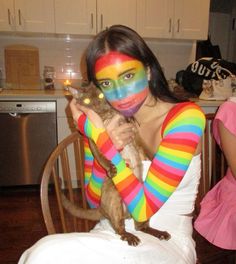 a woman with painted face and body holding a cat in her arms while sitting on a chair