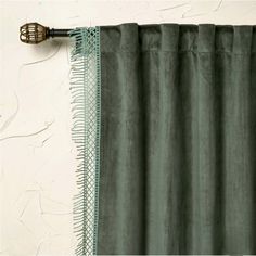 a green curtain hanging on the side of a white wall next to a metal hook