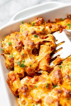 a white casserole dish filled with cheesy pasta and meat, garnished with parsley