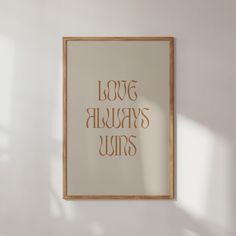 a white wall with a wooden frame hanging on it and the words love always wins