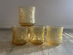 three yellow glass tumblers sitting on top of a wooden table next to each other