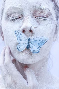 a woman is covered in white powder with a blue butterfly on her nose and face