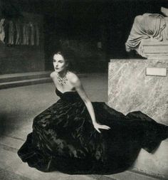 black and white photograph of woman in evening dress sitting on the floor next to a statue