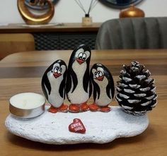 three penguins sitting on a rock next to a pine cone with a candle in the middle