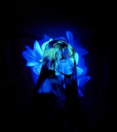 a woman with long hair standing in front of a blue flower on a black background