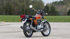 an orange and black motorcycle parked in a parking lot next to some yellow dandelions